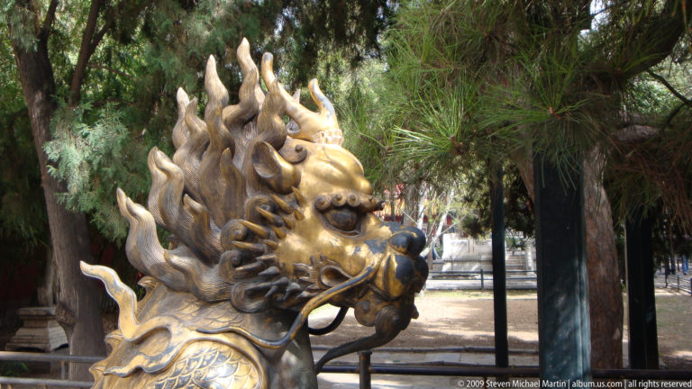 Close-up of the horned head and flame-like mane of a gilt-bronze qilin or dragon-like auspicious guardian sculpture with a metal ring in its mouth in the Forbidden City.