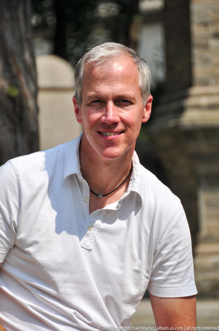 Gray-haired male visitor in a white shirt looking toward the camera at the Giant Wild Goose Pagoda temple grounds in Xi'an.