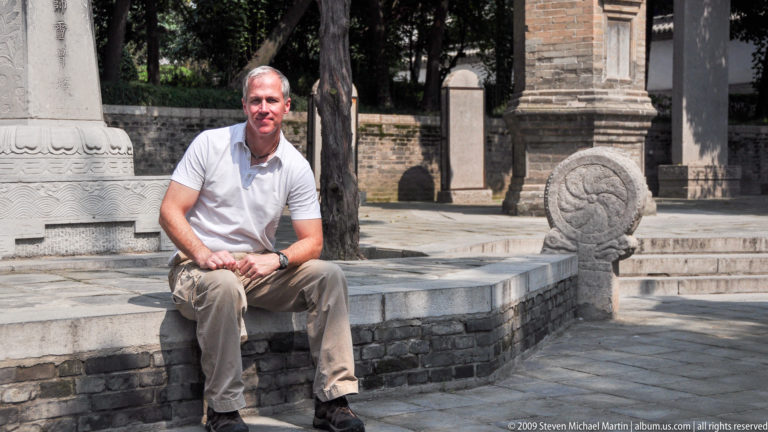 Male visitor seated on a low stone ledge beside carved stone markers in a paved courtyard at Da Ci'en Temple.