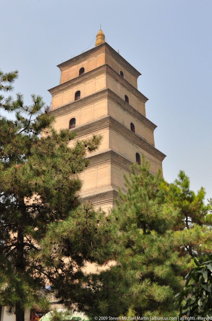 Upper tiers of the Giant Wild Goose Pagoda seen through dense green pine branches in Xi'an.