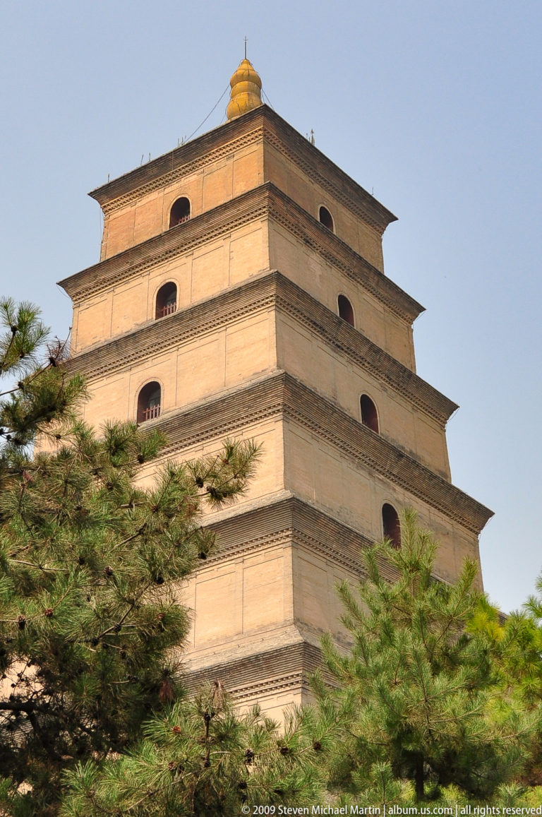 Oblique upper-tier view of the Giant Wild Goose Pagoda rising behind pine branches, showing several stepped brick tiers with arched openings.