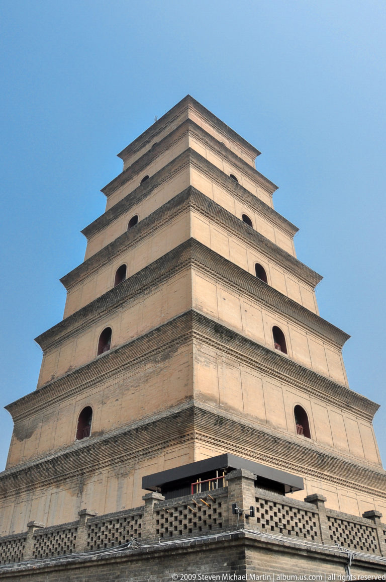 Oblique close view of the Giant Wild Goose Pagoda’s upper brick tiers with arched openings and projecting cornices against a clear blue sky.