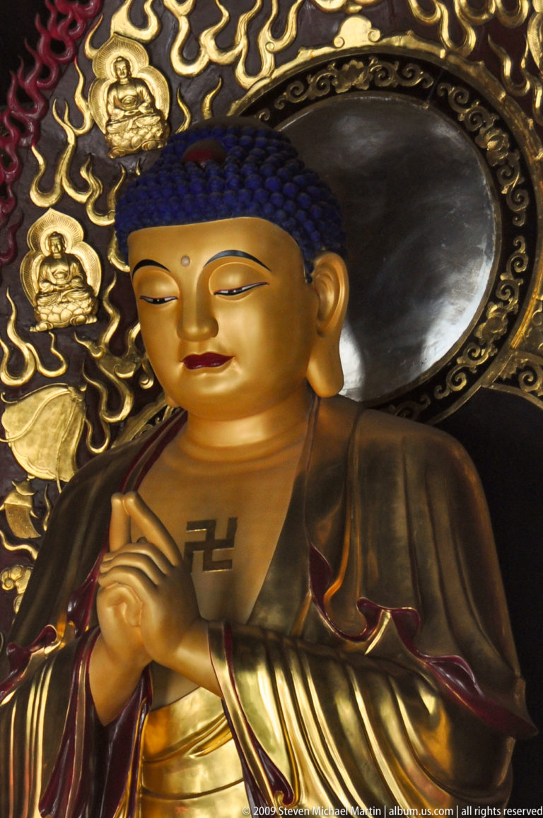 Close view of a gilded Buddha’s face with halo and a left-facing Buddhist swastika symbol on the chest.