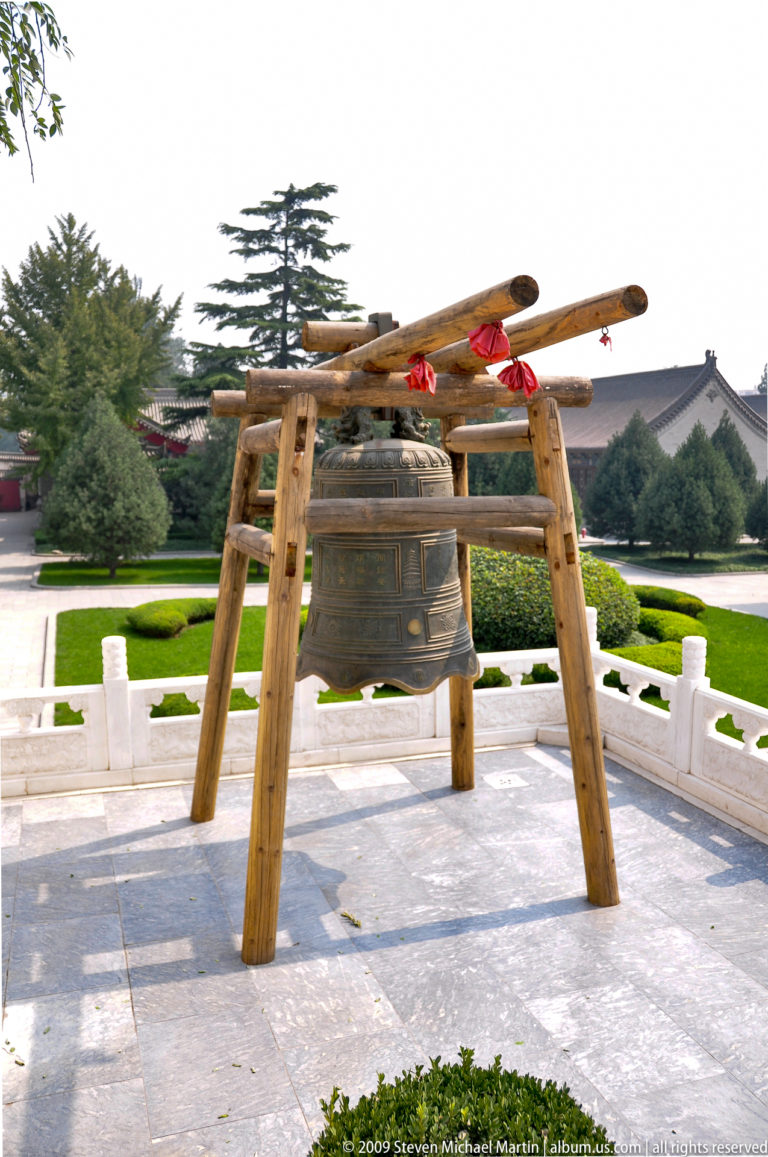 Large cast bronze temple bell hanging from a rustic timber frame with red ribbons at Da Ci'en Temple in the Giant Wild Goose Pagoda complex, Xi'an.