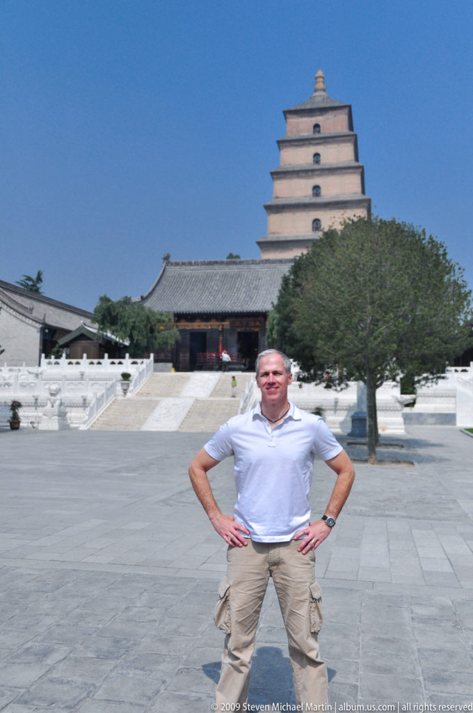 Male visitor standing in the central courtyard of Da Ci’en Temple with a temple hall and the Giant Wild Goose Pagoda rising behind him.