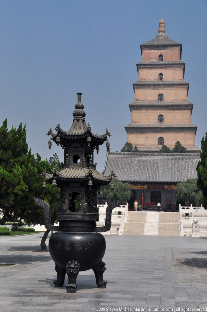 Multi-tiered pavilion with upturned eaves and hanging bells in front of a gray-tiled hall and the Giant Wild Goose Pagoda at Da Ci’en Temple in Xi’an.