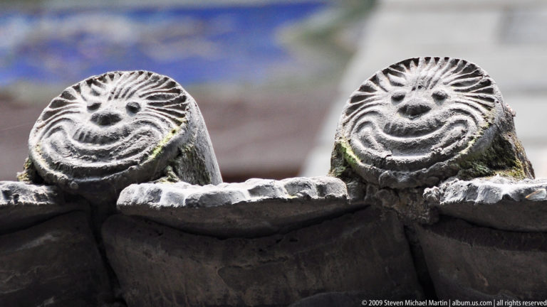 Close-up of weathered gray ceramic roof tiles with circular, radiating end motifs on a traditional Chinese temple roof.