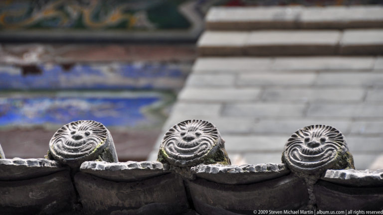 Three gray circular ceramic tile ends evenly spaced along the lower edge of a Da Ci'en Temple roof.