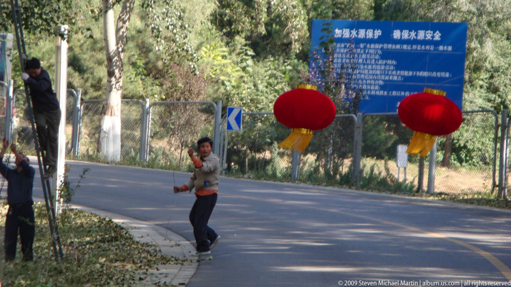 Performer beside a road at the Great Wall visitor area manipulating two large red lantern-shaped props suspended in motion.