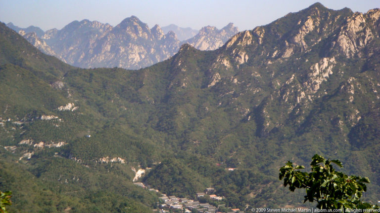 Forested, rocky mountains in the Beijing region with a small settlement in the valley below, part of the landscape surrounding the Great Wall area.