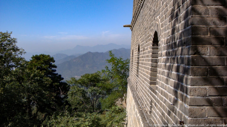 Side view of a brick Great Wall watchtower with a single arched window, overlooking distant mountain valleys.