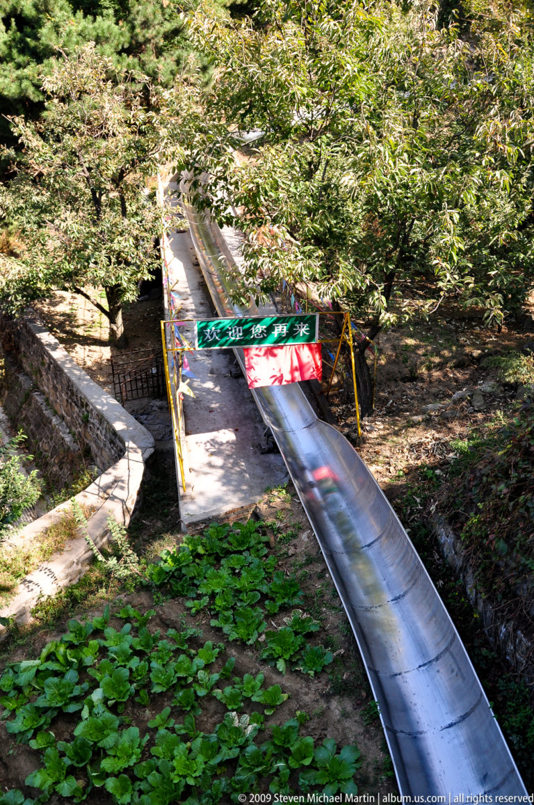 Upper entrance to the stainless-steel alpine slide at the Mutianyu Great Wall visitor complex, with a Chinese welcome banner above the chute.
