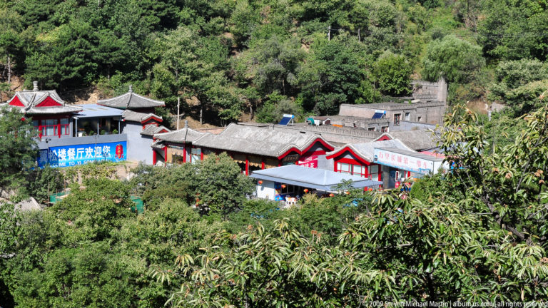 Red-trimmed, gray-tiled visitor-service buildings nestled in dense forest below the Mutianyu Great Wall.