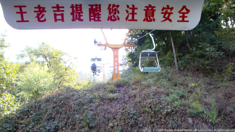 Open chairlift traveling above a steep forested hillside at Mutianyu, providing modern access toward the Great Wall.
