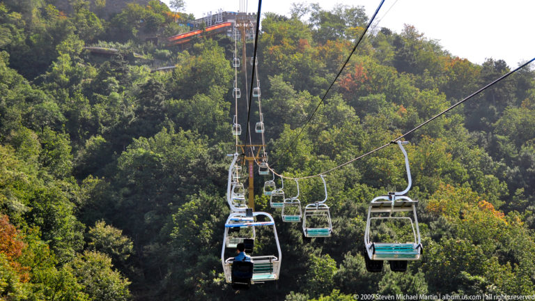 Open chairlift carrying visitors over forested terrain near the Mutianyu Great Wall access area.