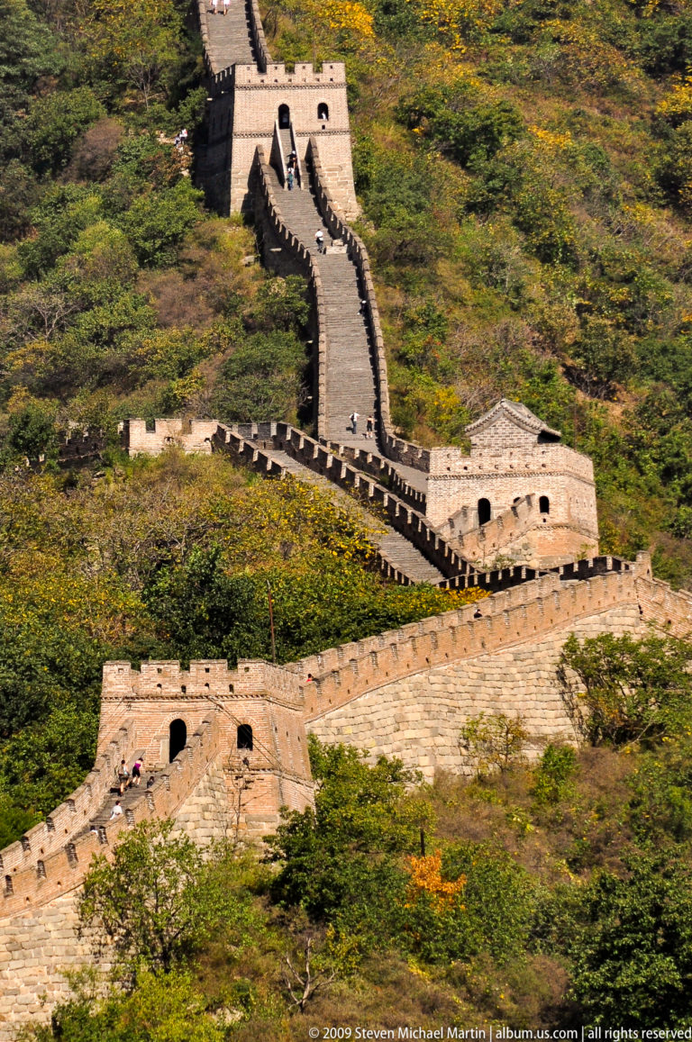 Telephoto view of closely spaced Great Wall watchtowers linked by very steep brick stairs along a forested mountain ridge at Mutianyu.