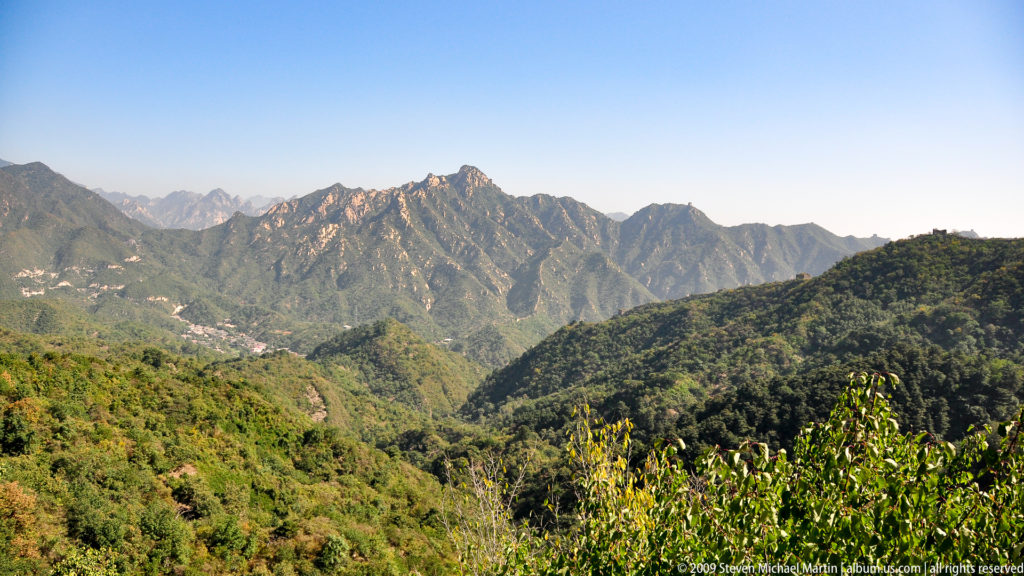 Panoramic view of rugged, forested mountain ridges near the Great Wall site under a clear sky.
