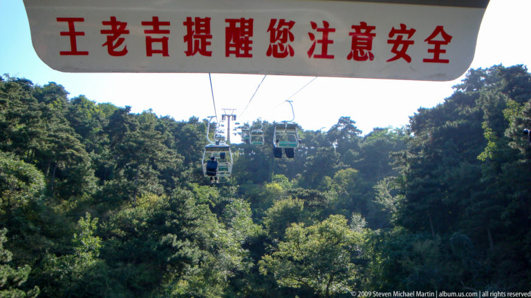 Modern open chairlift passing over a densely forested hillside at Mutianyu.