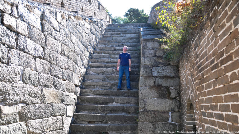 Single visitor standing on a narrow landing between steep Great Wall steps and high brick walls at Mutianyu.