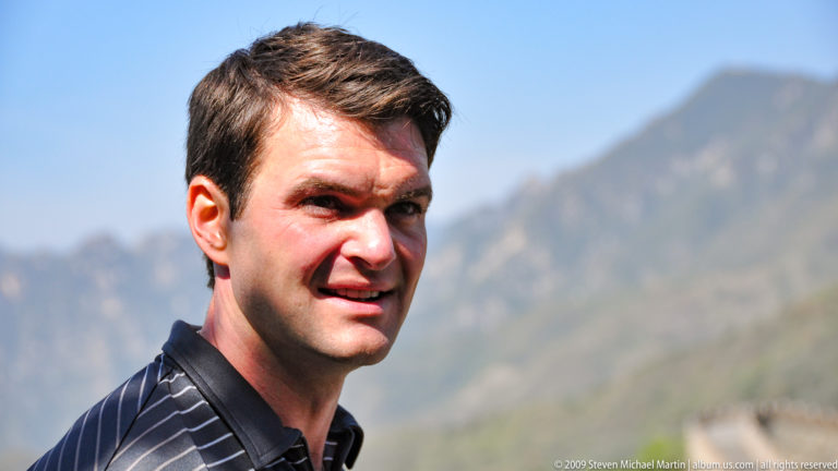 Close travel portrait of a male visitor at the Great Wall with an out-of-focus mountain ridge in the background.