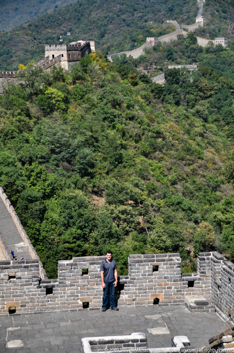 Partial edge of the Great Wall at Mutianyu with a visitor’s head visible above a steep, densely forested mountainside.