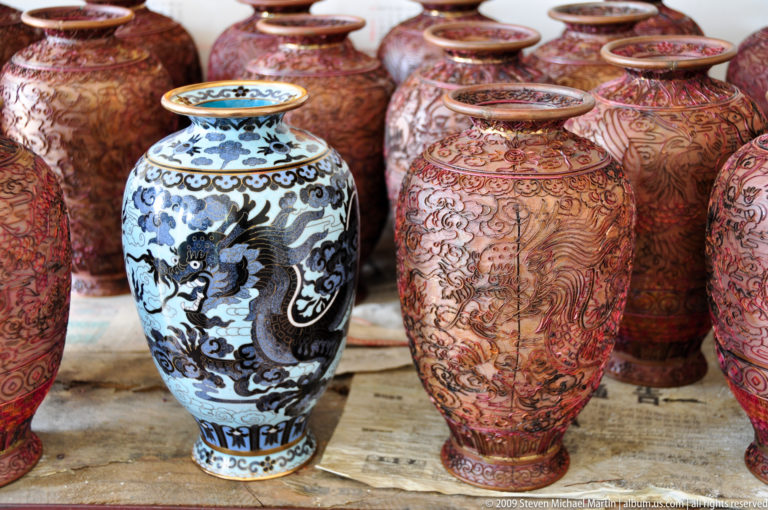 Close-up of contemporary souvenir ceramic vases, featuring a central blue-and-white dragon design surrounded by taller red and brown floral patterns.