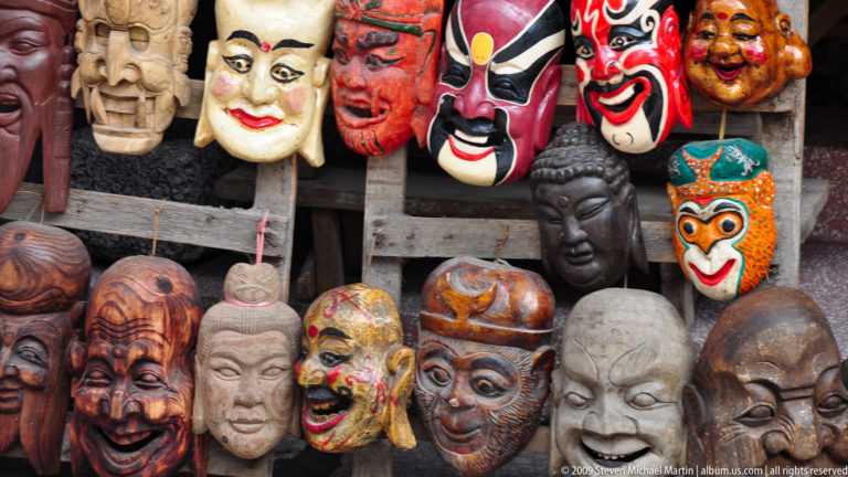 Rows of Chinese opera, Buddhist, and folk-style masks hanging for sale in a Yangshuo market.