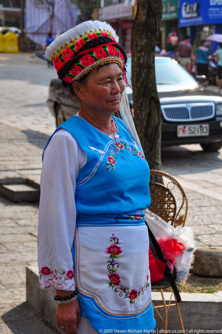 Close-up of a blue floral-embroidered vest with pink and green flowers and contrasting white sleeves worn by a woman in Guilin, China.