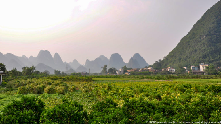 Cultivated fields on a flat plain leading toward layered karst peaks in hazy Guilin countryside.
