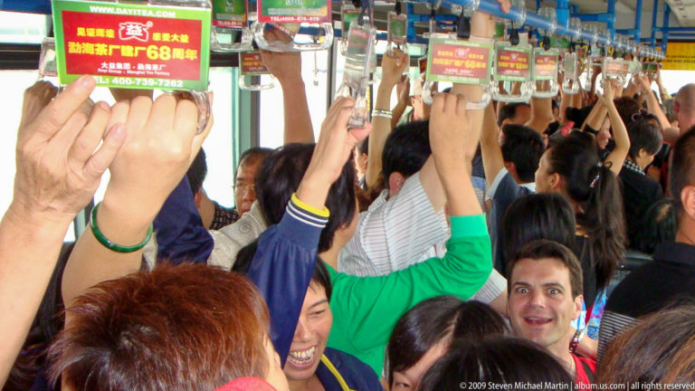 Young traveler standing among tightly packed passengers holding overhead straps on a crowded Guilin bus.