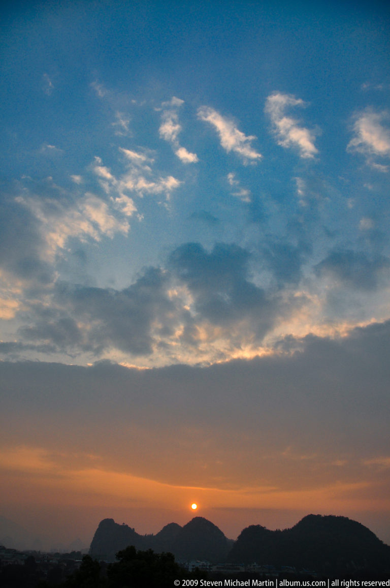 Backlit evening clouds over Guilin at dusk with warm light breaking through gaps near the horizon.