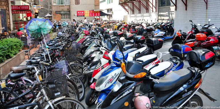 Tightly packed rows of bicycles, electric bikes, and scooters filling a parking area beside a building in Guilin.