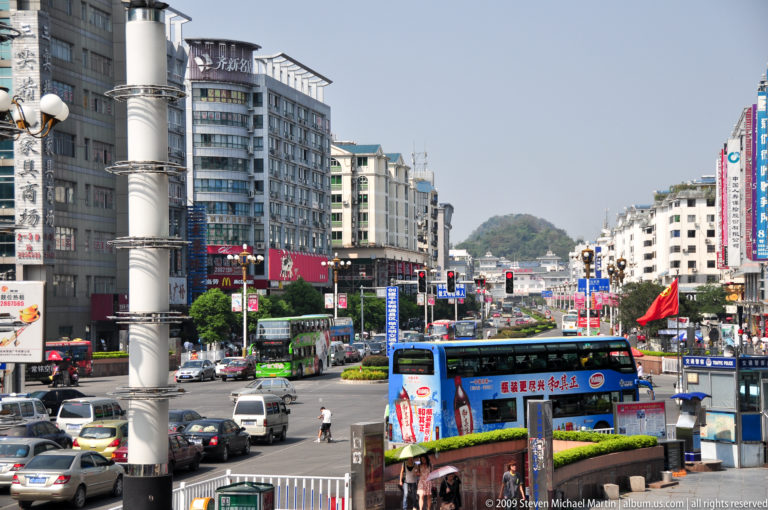 Downtown Guilin boulevard with cars and a blue double-decker bus driving toward a karst hill at the end of the street.