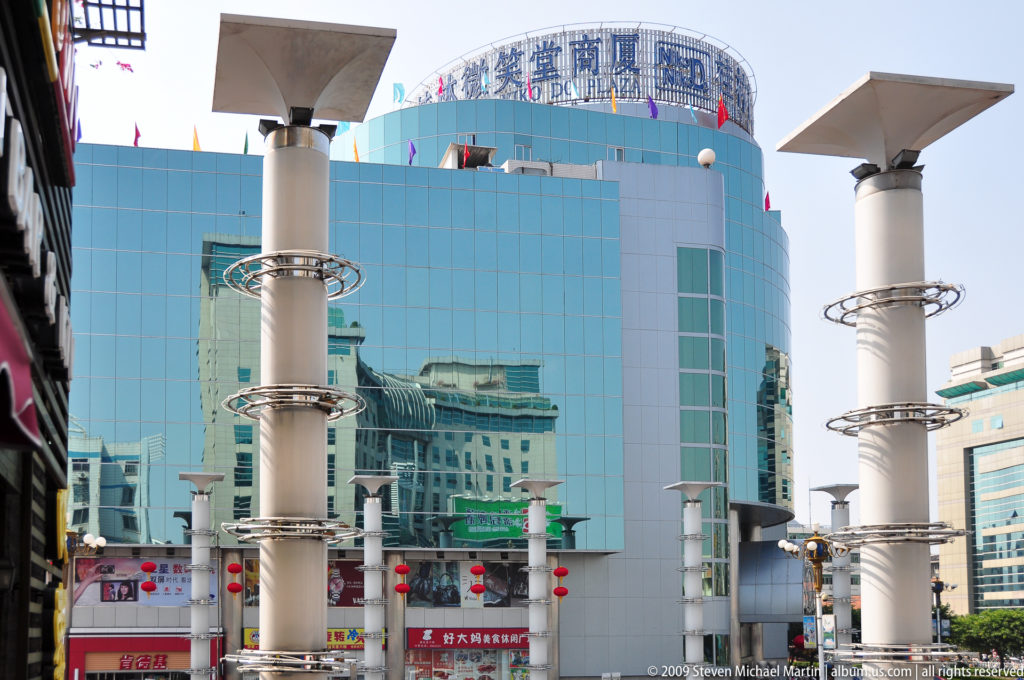 Curved turquoise-glass department store in central Guilin, with Chinese characters on the roofline and white columns with circular metal rings in front.