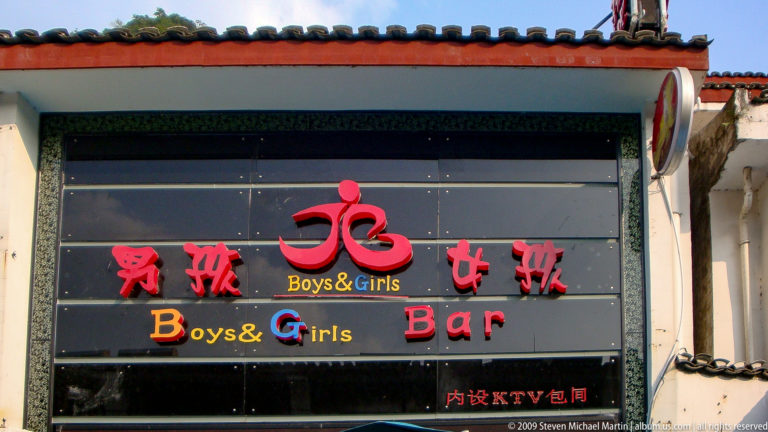 Bilingual “Boys & Girls Bar” sign with red Chinese and English text on a black facade in Yangshuo.