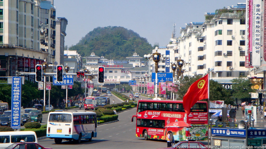 Divided boulevard in Guilin with buses and a landscaped median leading toward a steep green karst hill.