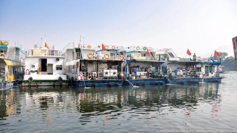 Several white and blue Li River passenger boats moored side by side at a Guilin cruise terminal, with reflections in the water.