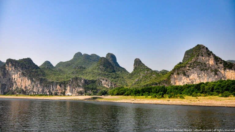 Wide bend of the Li River flowing beside pale limestone cliffs with exposed gravel bars along the banks.