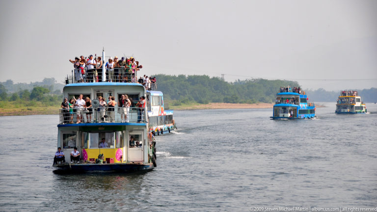 Passenger cruise boats in convoy on the Li River, with tourists standing on the open upper decks.
