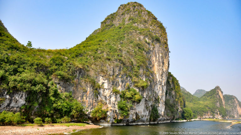 Isolated sheer limestone karst tower rising from the edge of the Li River.