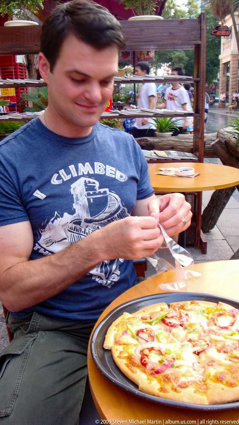 Traveler in a blue T-shirt putting on a clear disposable glove at an outdoor restaurant table in Guilin.