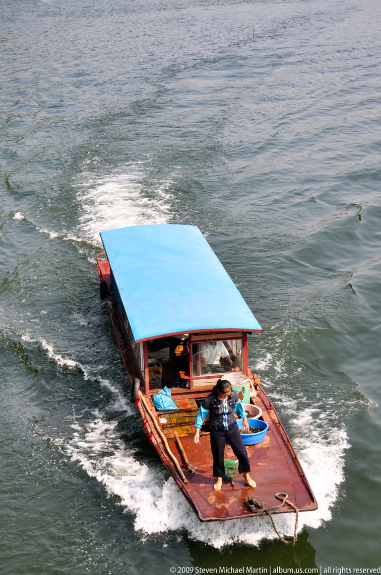Small blue-roofed motorboat following in the wake of a larger vessel on the Li River near Guilin.