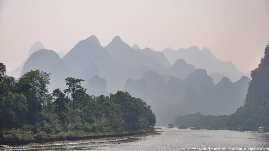 Li River with cruise boats traveling between hazy, layered karst mountains.