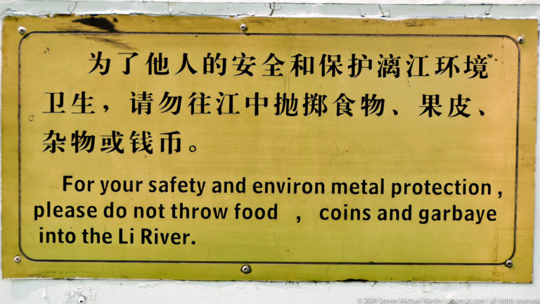 Yellow bilingual sign by the Li River asking visitors not to throw food, coins, or garbage into the water for safety and environmental protection.