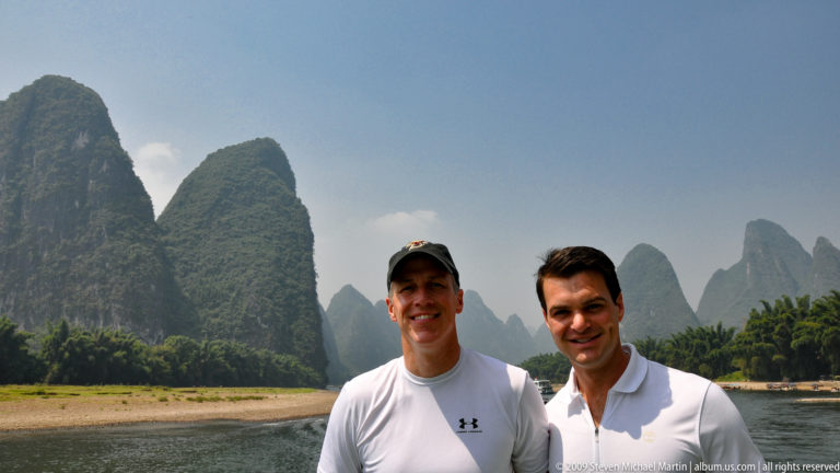 Two travelers standing together on a Li River boat with karst mountains rising in the background.
