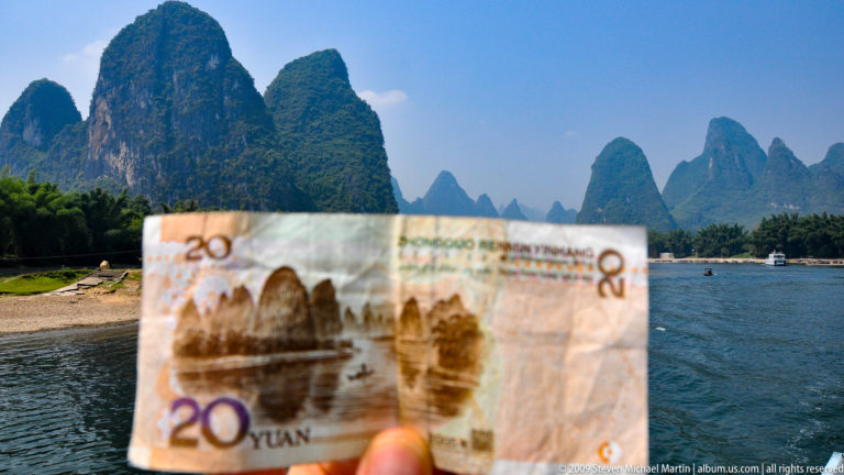 Hand holding a 20-yuan banknote against the matching Li River karst landscape in Guilin.