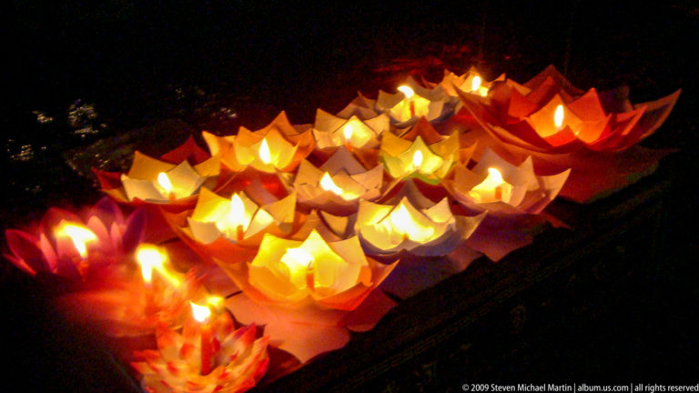 Cluster of floating paper lotus lamps with small flames on dark water in Lijiang, Yunnan, China.