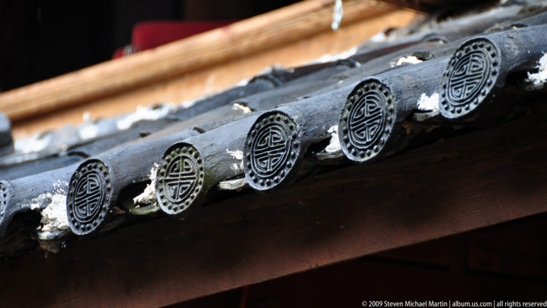Close-up of circular grey tile-end ornaments with longevity-style geometric motifs beneath a weathered roof edge in Lijiang, Yunnan, China.
