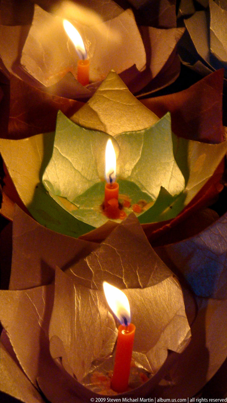 Close-up of a small red candle burning inside a folded paper lotus with green and pale petals in Lijiang, Yunnan, China.