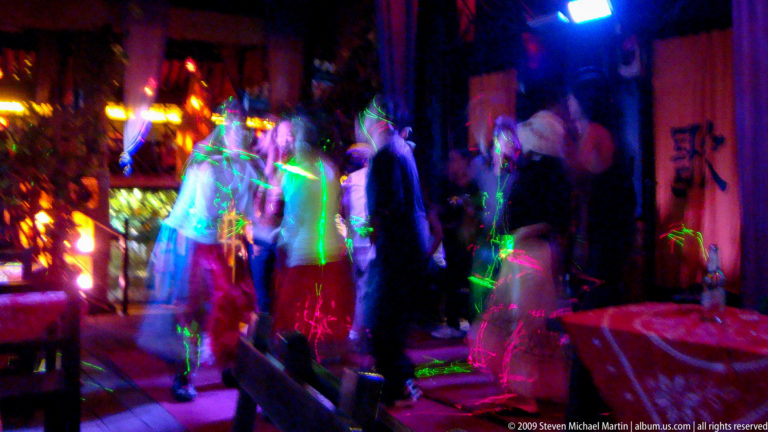 Blurred dancers under green and blue laser and stage lights in a nightclub in Lijiang, Yunnan, China.